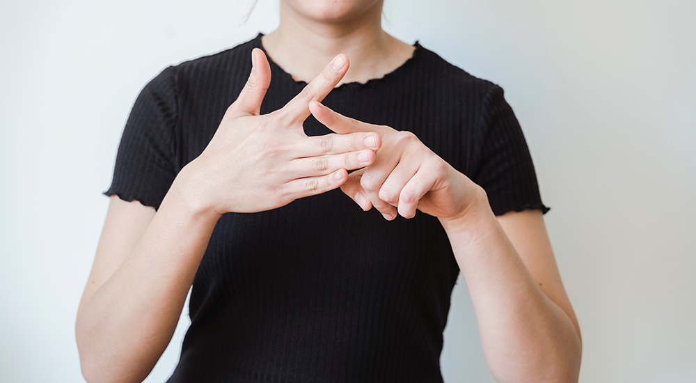 Sie sehen eine junge Frau die in Gebärdensprache spricht. Bei Hörschädigungen kann die Gebärdensprache in Lernsystemen Barrieren minimieren.